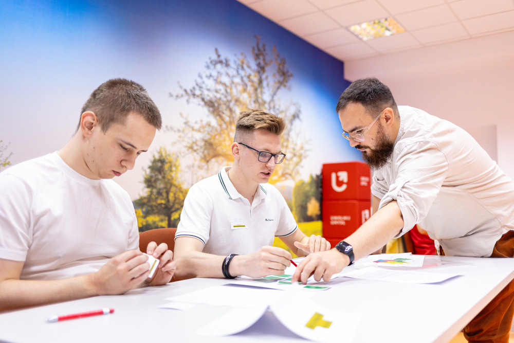 dwoje studentów siedzących przy stole dyskutuje z trenerem
