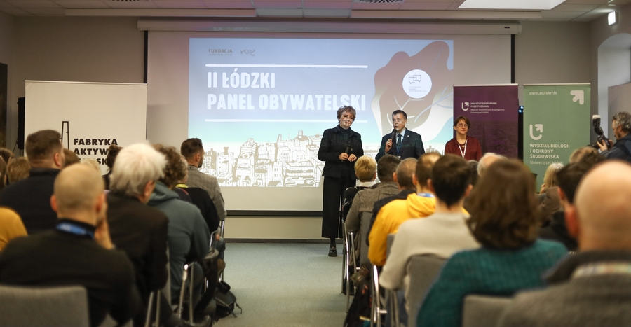 Trzy osoby z mikrofonami przed publicznością