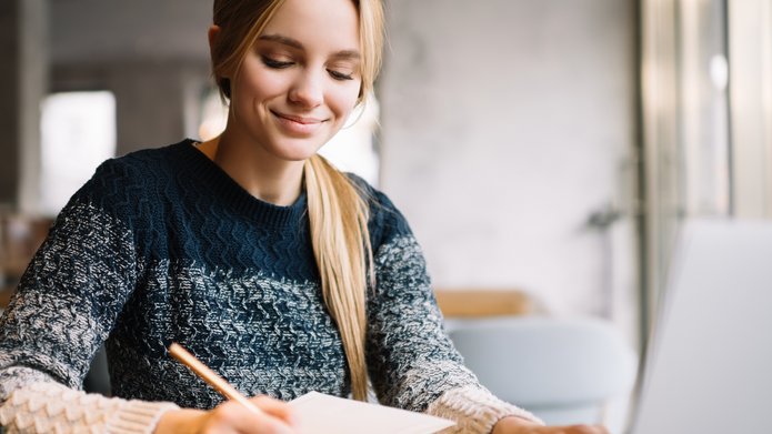 Na zdjęciu dziewczyna sporządza notatki przed komputerem