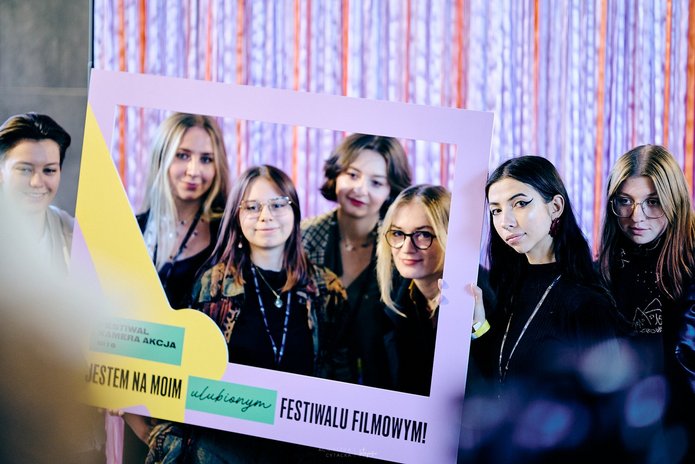 Grupa młodych osób pozuje do zdjęcia z ramką promocyjną Festiwalu Kamera Akcja 