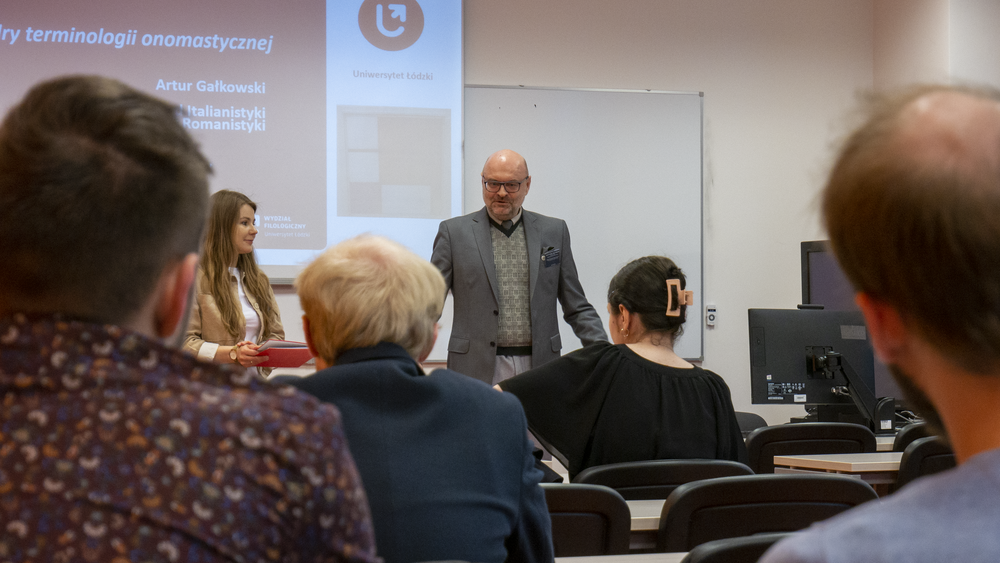 zdjęcie przedstawia osoby siedzące w sali i stojącego wykładowcę, dr. hab. prof. UŁ Artura Gałkowskiego
