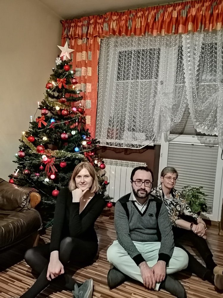 Participants of the University of Lodz "Christmas Guest" campaign, three people sitting under the Christmas tree